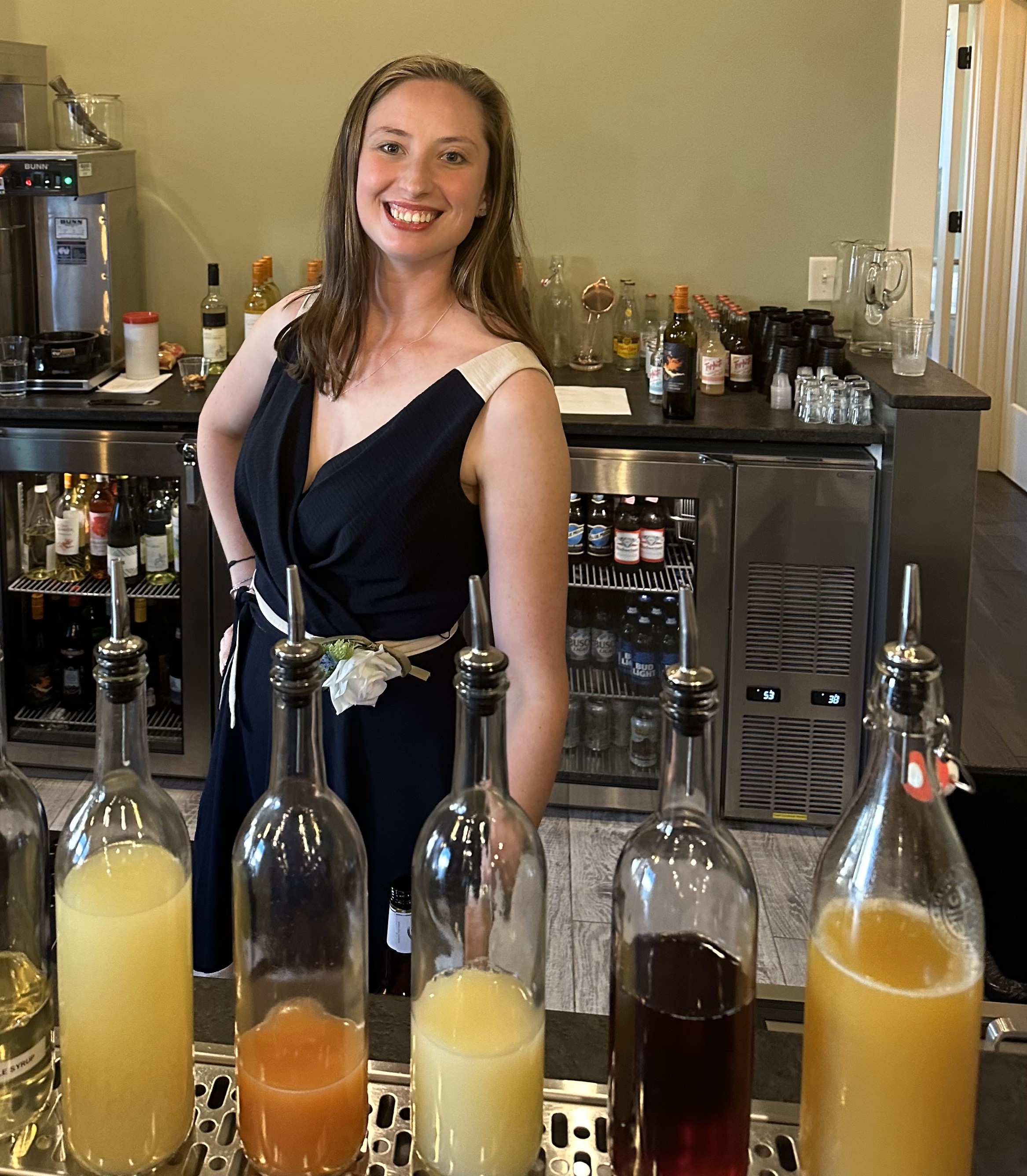 A woman in a dress standing behind a bar smiling